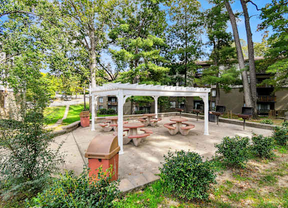 A picnic area with tables and a pavilion is surrounded by trees.