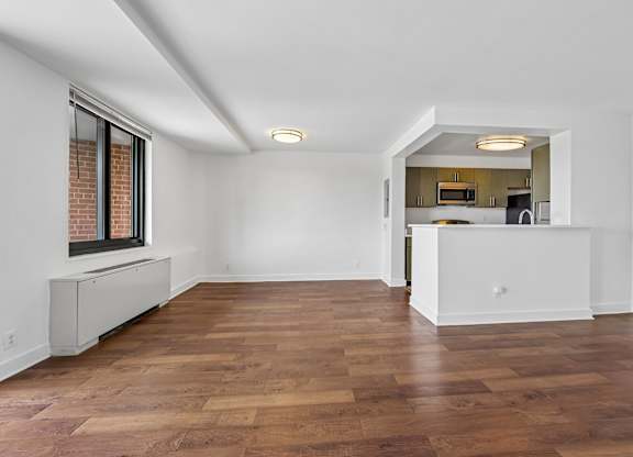 A room with wooden floors and a kitchen area in the back.