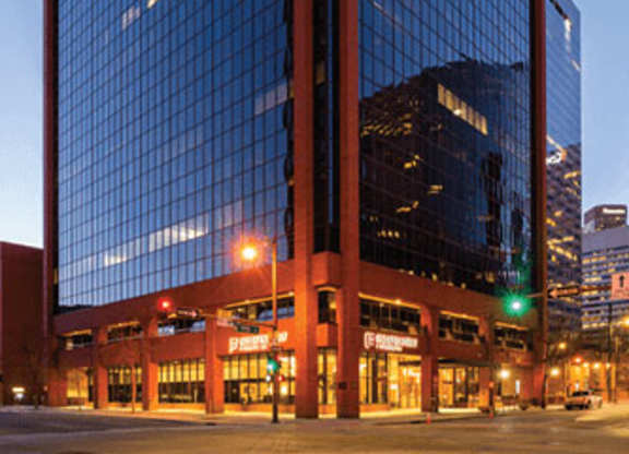 A tall glass building with a red frame stands in the evening sunlight.