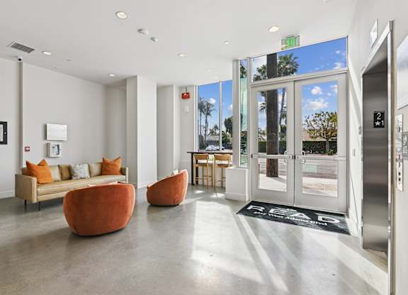 A white hallway with a couch and two orange chairs.