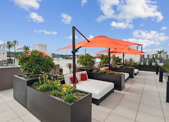 A patio with a white couch and a red umbrella.