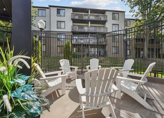 A patio with white chairs and a table is in front of a building.
