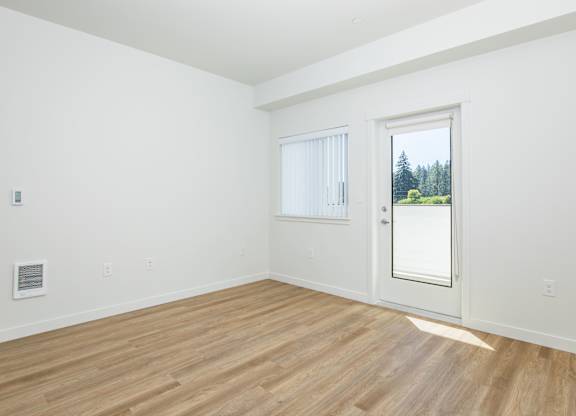 A room with a wooden floor and a door leading to a balcony with a view of trees.