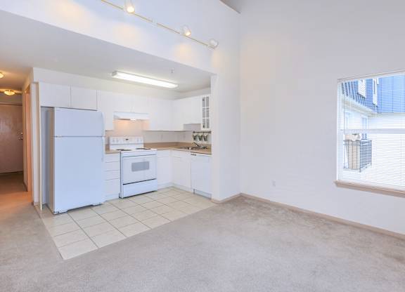 A kitchen with white appliances and a window with blinds.