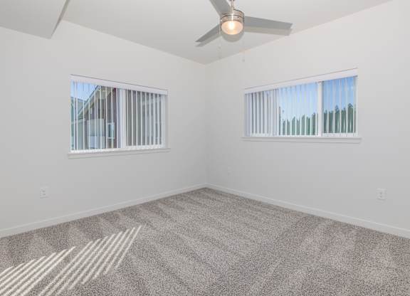 A room with a ceiling fan and two windows.