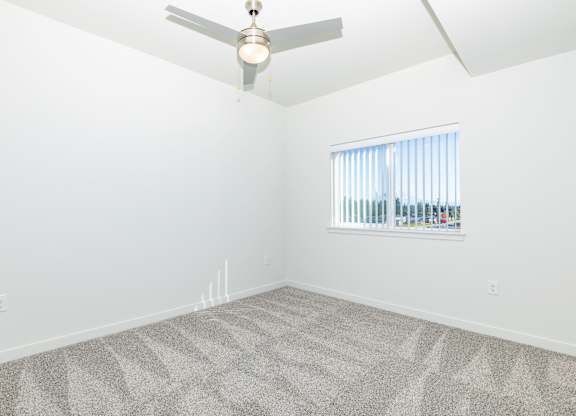 A room with a ceiling fan and a window with blinds.