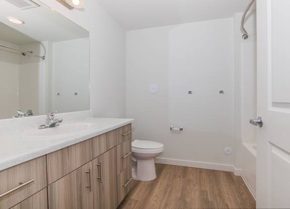 A white bathroom with wooden floors and a white toilet.