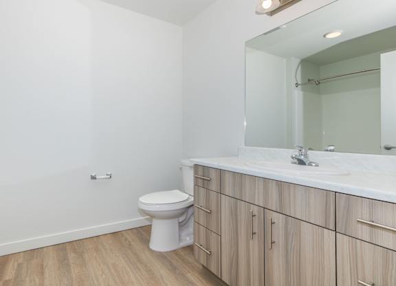 A white toilet sits in a bathroom with wooden floors and a white sink.