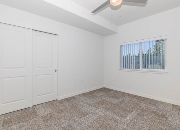 A room with a carpeted floor, a ceiling fan, and a window with blinds.