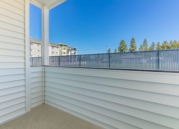 A balcony with white walls and a black railing overlooks a residential area.