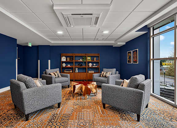A room with blue walls and a carpeted floor with a wooden bookshelf and grey chairs.