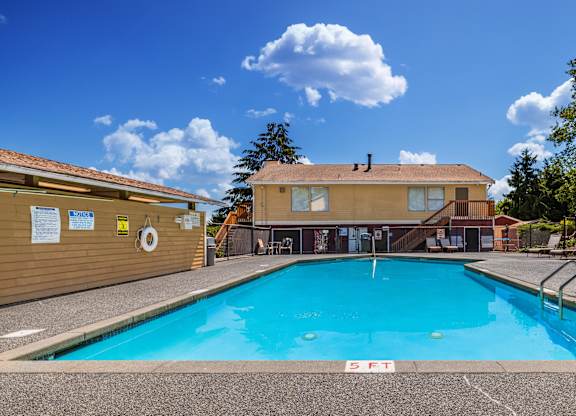 A large swimming pool in front of a building with a blue sky and clouds in the background.