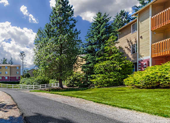 A road leads to a building with a white fence and trees in the background.