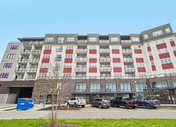 A large building with red and white balconies is surrounded by parked cars.