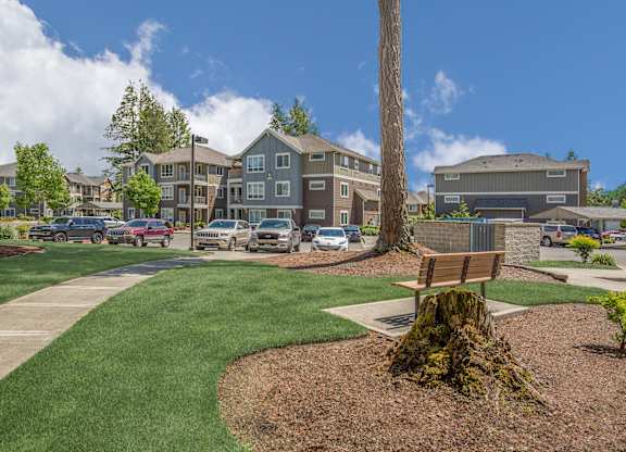 A park with a bench and a tree stump in the foreground.