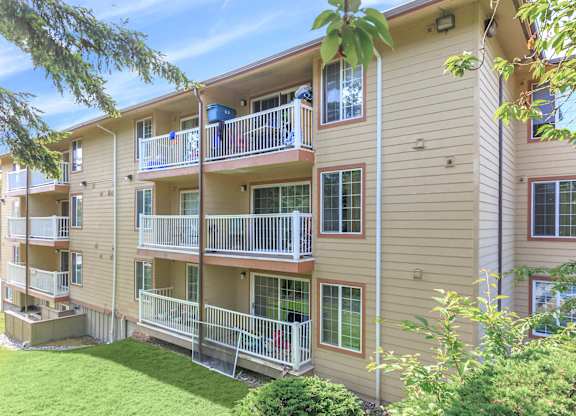 Apartment building with balconies and greenery in front.