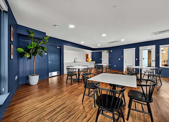A room with blue walls and wooden floors has a long white table surrounded by black chairs.