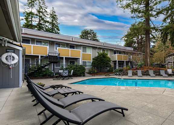 A pool surrounded by lounge chairs in front of apartment buildings.