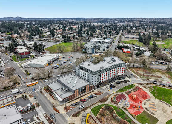 A large building with a red roof is surrounded by a parking lot and a playground.