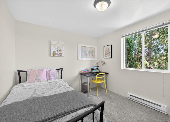 A bedroom with a bed, desk, chair, and pictures on the wall.