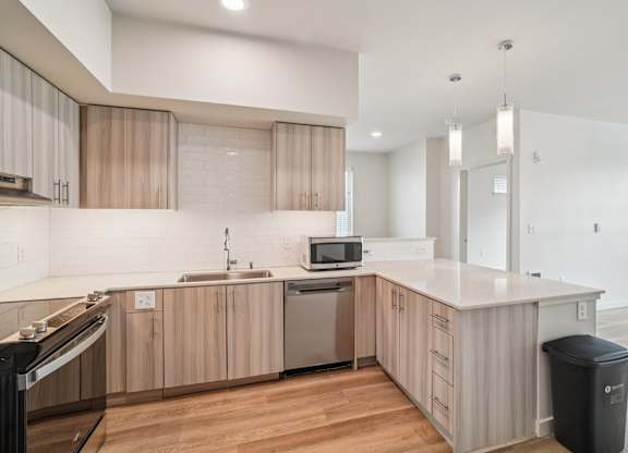 A modern kitchen with wooden cabinets and a black trash bin.