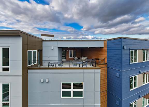 A modern multi-story building with a balcony and a blue sky with clouds in the background.