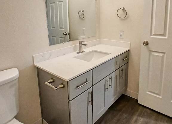 A bathroom with a white toilet, a sink with a cabinet underneath it and a mirror above the sink.