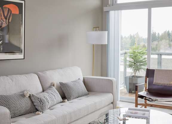 A grey couch with two pillows and a small table with a lamp on it.