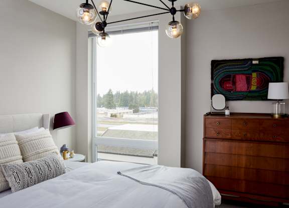 A bedroom with a large bed, a wooden dresser, and a window overlooking a parking lot.