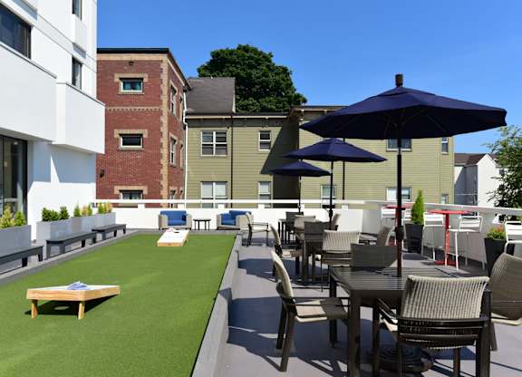 Tacoma, WA, Pet-Friendly Apartments - The Orion - Rooftop Patio With Outdoor Seating, Turf Game Area, Umbrellas, Planters, and Expansive City Views.