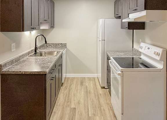 A kitchen with a white refrigerator and a sink with a granite countertop.