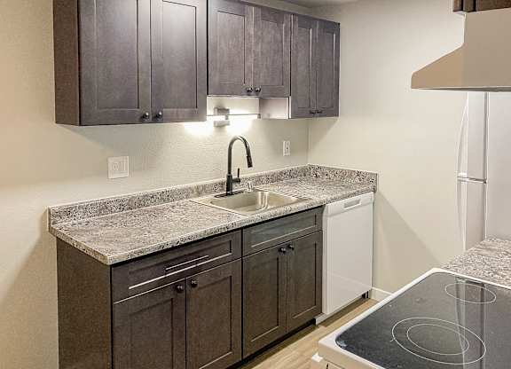 A kitchen with a granite countertop and dark brown cabinets.