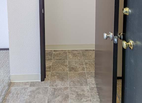 A black door with a gold handle is open to a hallway.