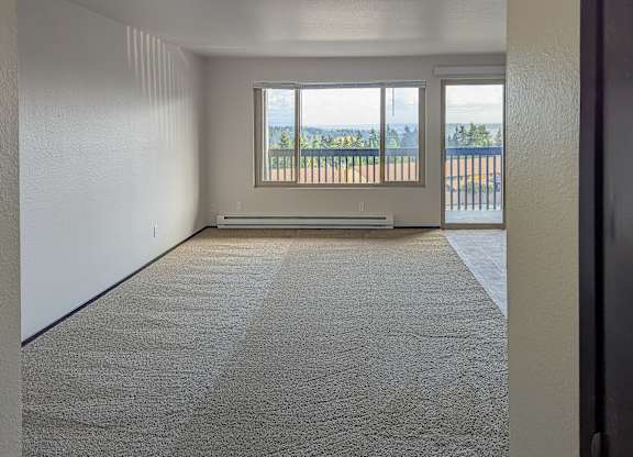 A room with a carpeted floor and a large window overlooking a balcony.