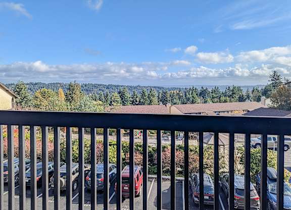 A view from a balcony overlooking a parking lot and a forest.