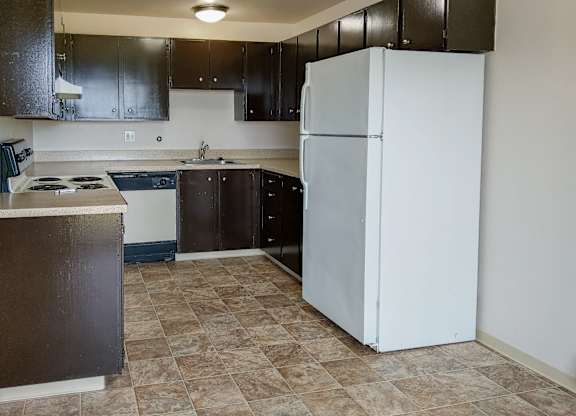 A kitchen with a white refrigerator and brown cabinets.
