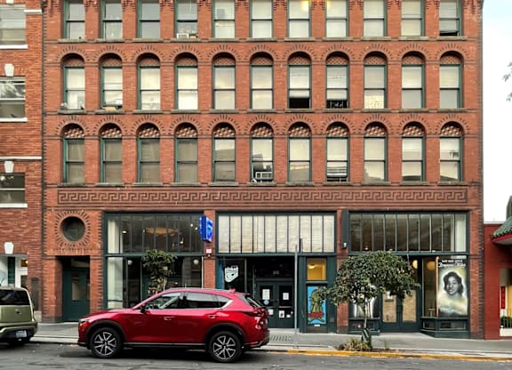 A red car is parked in front of a red brick building.