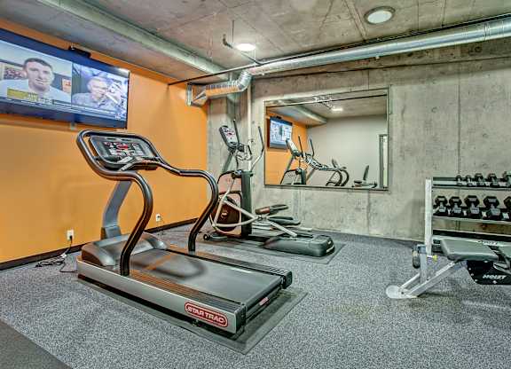 A treadmill in a gym with a TV screen showing two people.