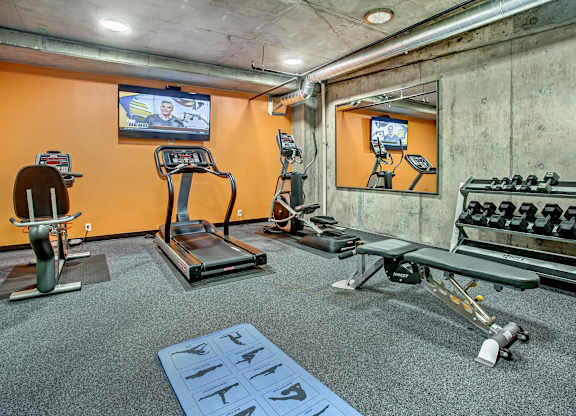 A gym with orange walls and a variety of equipment including treadmills, exercise bikes, and weight machines.
