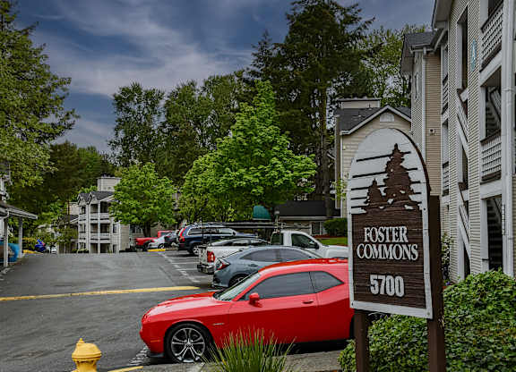 A red car is parked in a parking lot with a sign that says