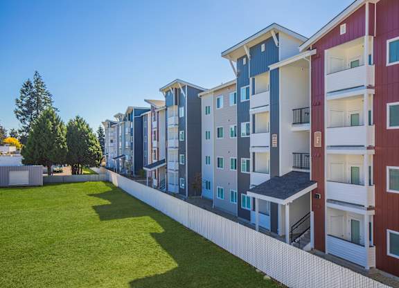 A row of modern apartment buildings with balconies and a green lawn in front.