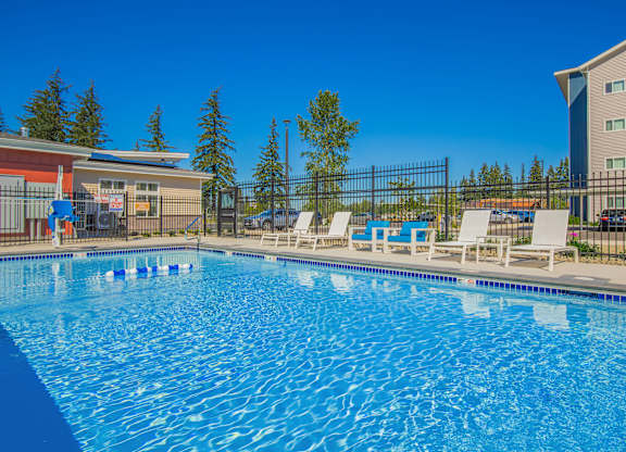 A large blue swimming pool with white lounge chairs and a fence around it.