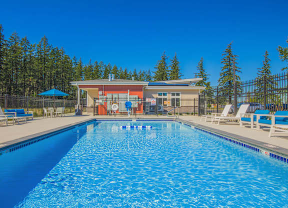 A large swimming pool with a blue umbrella and lounge chairs.