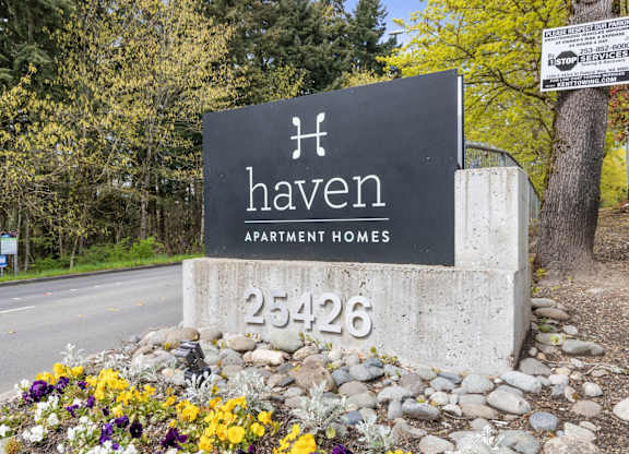 A sign for Haven Apartment Homes is surrounded by flowers and rocks.