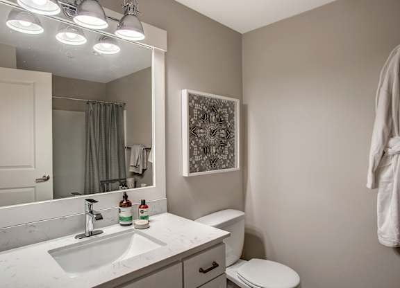A bathroom with a toilet, sink, mirror, and a picture on the wall.