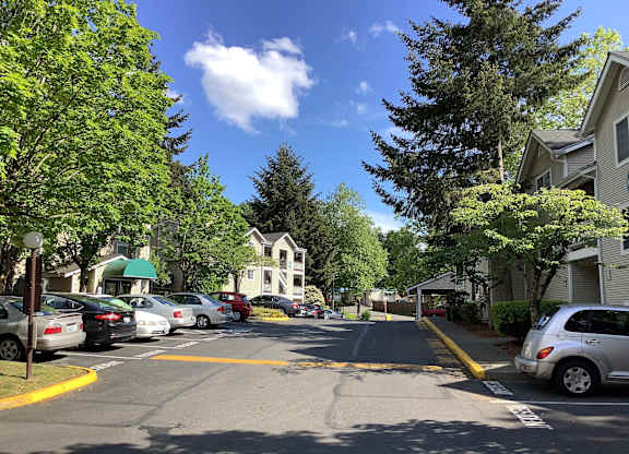 A street view with cars parked on the side and a white building in the background.