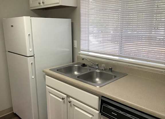 A white refrigerator stands next to a sink in a kitchen.