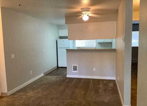 A kitchen area with a refrigerator, cabinets, and a ceiling fan.