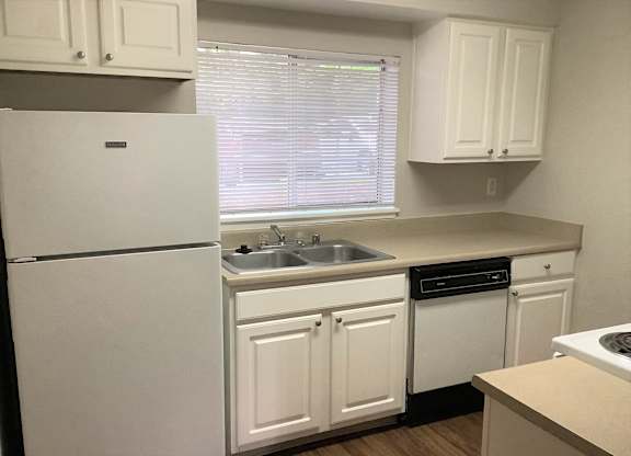 A white refrigerator stands in a kitchen with white cabinets and a window with blinds.