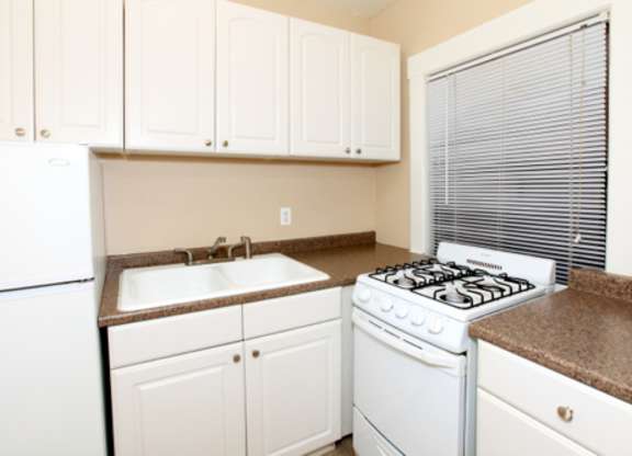 A white kitchen with a white fridge, white stove, and white cabinets.